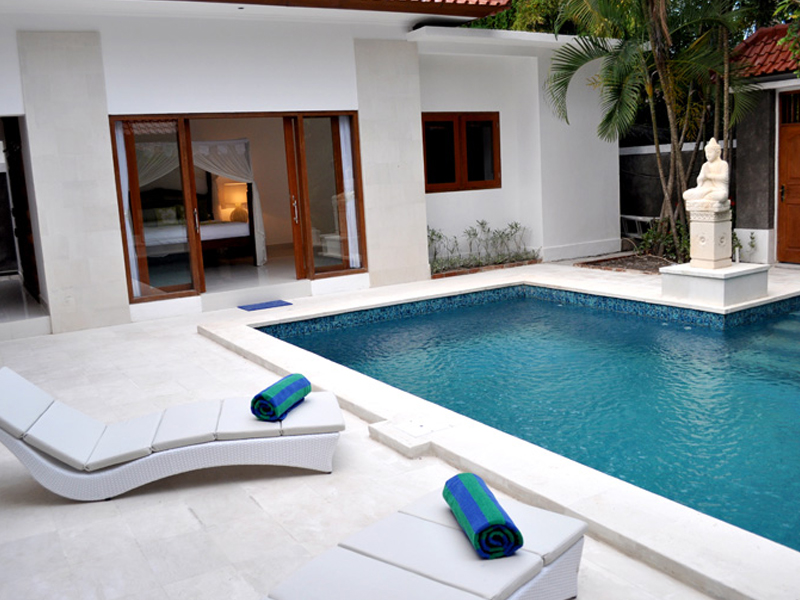 A pool with two white lounge chairs and a fire place.