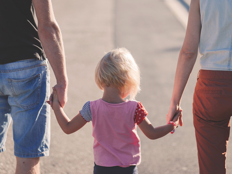 A little girl holding hands with two adults.